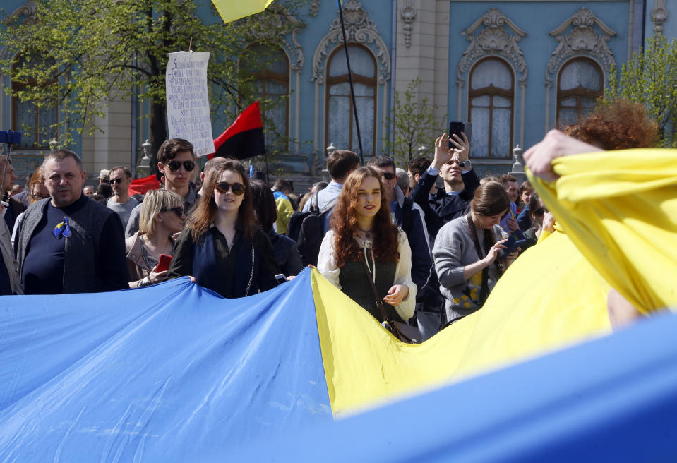 People hold Ukrainian national flag in front of the parliament in capital Kiev, Ukraine, Thursday, April 25, 2019. Ukrainian lawmakers voted a draft law on the Ukrainian language, which provides for the mandatory use of the national language by government agencies, local self-government and in other spheres of public life. (AP Photo/Efrem Lukatsky)