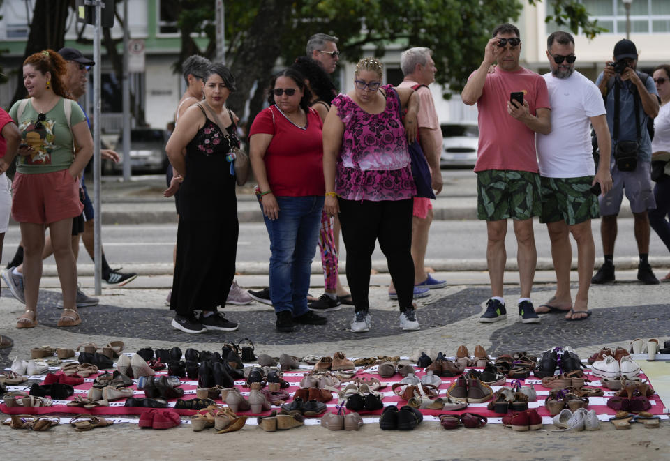 Los transeúntes observan una instalación compuesta por los nombres de las víctimas de la violencia de género y zapatos de mujer donados, exhibida en el borde de la playa de Copacabana para conmemorar el Día Internacional de la Eliminación de la Violencia contra la Mujer, en Río de Janeiro, Brasil, el sábado 25 de noviembre, 2023. (Foto AP/Silvia Izquierdo)