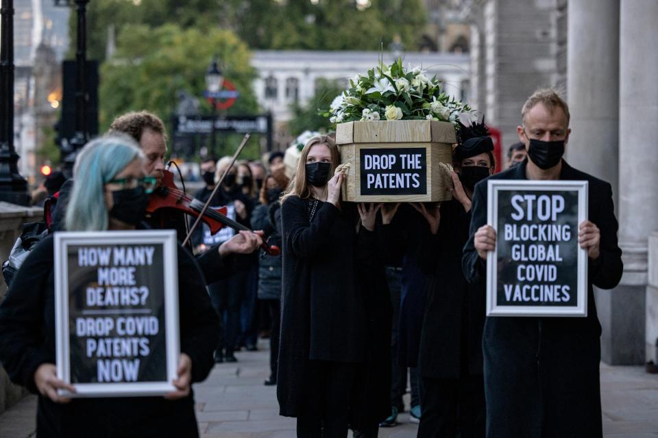 A crowd of people carry a coffin with signs that read "Drop the Patent" and "Stop blocking global Covid vaccines"