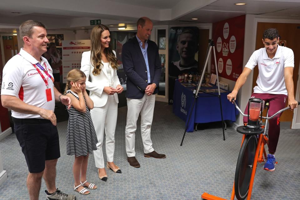 Tim Lawler CEO of SportsAid, Princess Charlotte of Cambridge, Catherine, Duchess of Cambridge and Prince William, Duke of Cambridge watch a demonstration of a bicycle powered smoothie maker during a visit to SportsAid House at the 2022 Commonwealth Games