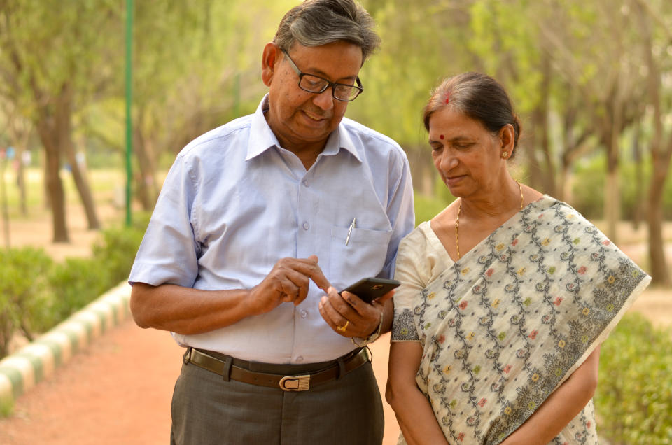 Senior retired man and woman couple in park looking at  their smart phone and laughing in Delhi, India