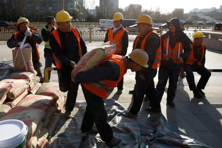 FILE PHOTO: A builder carries a sack of cement in central Beijing