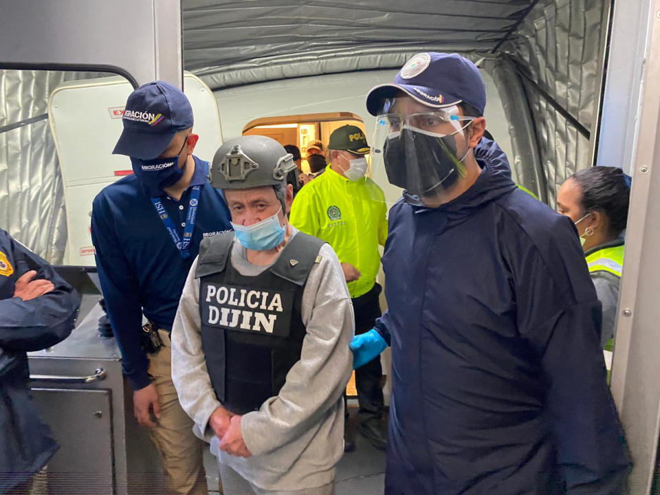 In this photo released by the Colombian Migration Press Office, ex-paramilitary commander Hernan Giraldo Serna, center, is escorted upon arrival at the El Dorado airport after being deported from the U.S. to Bogota, Colombia, Monday, Jan. 25, 2021. Giraldo, 74, was deported from the U.S. and immediately taken into custody by authorities in Colombia, where he is expected to serve time for crimes against humanity, including torture, displacement, sexual slavery and kidnapping, as well as drug trafficking. (Colombian Migration Press Office via AP)