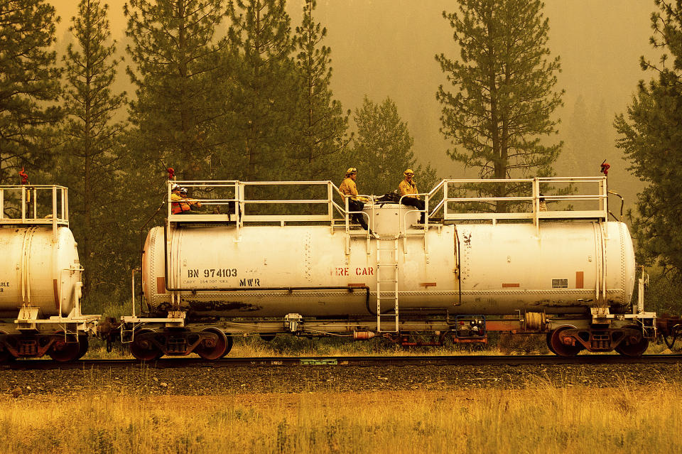 Firefighters ride atop a fire train while battling the Dixie Fire in Plumas County, Calif., on Saturday, July 24, 2021. The train is capable of spraying retardant to coat tracks and surrounding land. (AP Photo/Noah Berger)