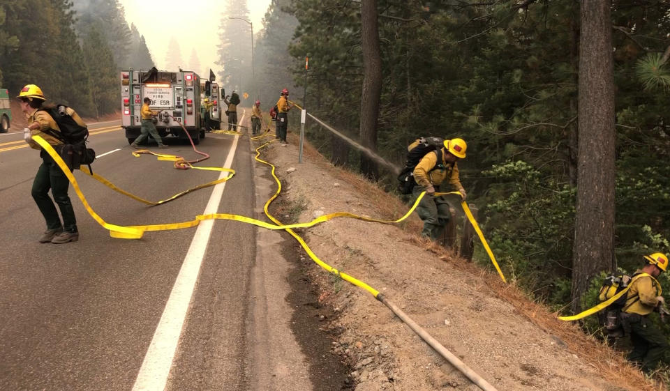 Fire crews carry a hose down a hill as the Caldor Fire burns on both sides of Highway 50 about 10 miles east of Kyburz, Calif., on Thursday, Aug. 26, 2021, as the fire pushes east prompting evacuation orders all the way to Echo Summit. The Caldor Fire, the nation's top priority for firefighting resources, grew to more than 213 square miles (551 square kilometers) southwest of Lake Tahoe but containment remained at 12%, according to the California Department of Forestry and Fire Protection. Climate change has made the West warmer and drier in the past 30 years and will continue to make the weather more extreme and wildfires more destructive, according to scientists. (Sara Nevis/The Sacramento Bee via AP)