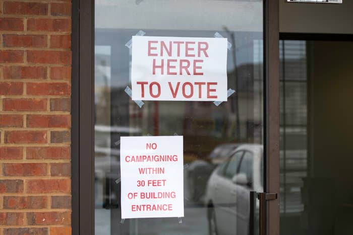 A door with two signs reading "ENTER HERE TO VOTE" and "NO CAMPAIGNING WITHIN 30 FEET OF BUILDING ENTRANCE"