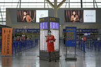 An airliner staff wearing a face mask to help curb the spread of the coronavirus stands near quiet check-in counters at Pudong International Airport in Shanghai, China, Sunday, July 25, 2021. Airline flights were canceled in eastern China and cargo ships were ordered out of the area Saturday as Typhoon In-fa churned toward the mainland after dumping rain on Taiwan. (AP Photo/Andy Wong)