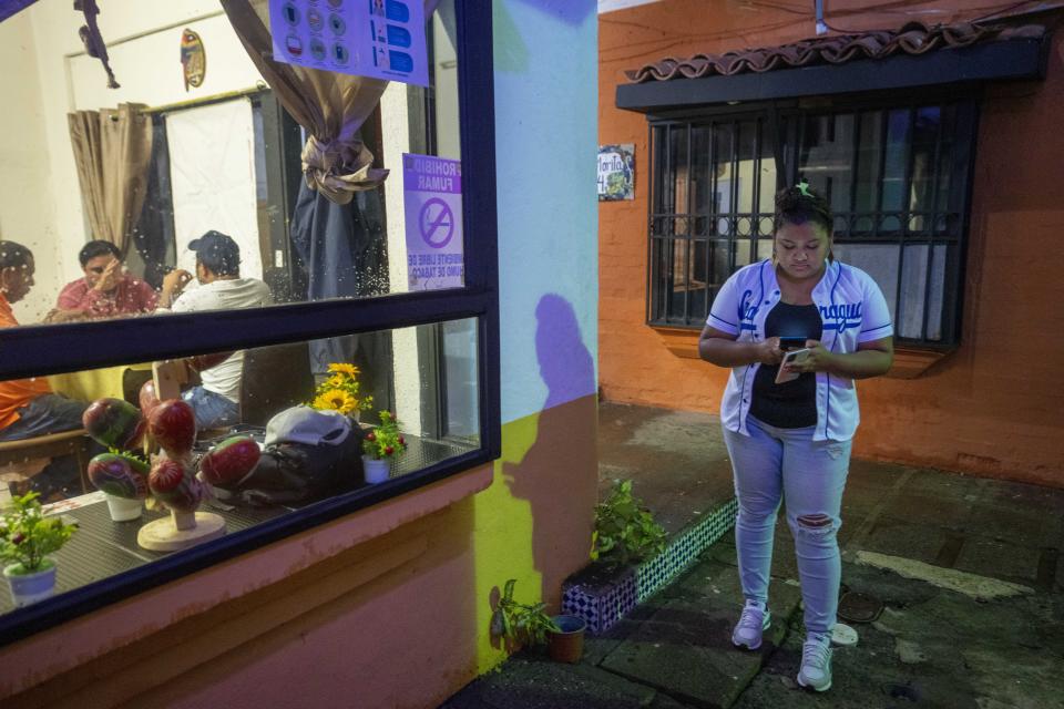 Nicaraguan asylum-seeker Evelyn Morales Cuningham checks her phone outside the diner she opened this year in San Jose, Costa Rica, Friday, Aug. 26, 2022. The 28-year-old said she quickly sold several of her businesses and home in Nicaragua in 2018 when she took her three children to Costa Rica and applied for asylum, where she continues to wait for approval. (AP Photo/Moises Castillo)