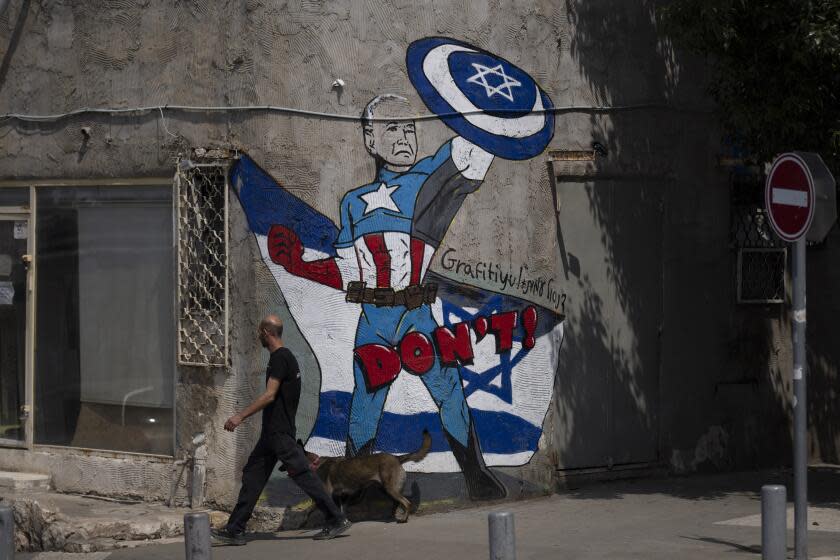 A man walks past a mural depicting the U.S. president Joe Biden as a superhero defending Israel on a street in Tel Aviv, Israel, Sunday, April 14, 2024. Israel on Sunday hailed its successful air defenses in the face of an unprecedented attack by Iran, saying it and its allies thwarted 99% of the more than 300 drones and missiles launched toward its territory. But regional tensions remain high, amid fears of further escalation in the event of a possible Israeli counter-strike. (AP Photo/Leo Correa)