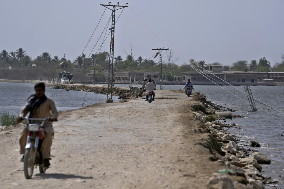 Motorcyclists drive through a dusty road surrounded by remaining water of last year's floods, near Therhi town in Khairpur, a district of Pakistan's Sindh province, Saturday, May 20, 2023. A year on from the floods in Pakistan that killed at least 1,700 people, destroyed millions of homes, wiped out swathes of farmland, and caused billions of dollars in economic losses, the country still hasn't fully recovered. (AP Photo/Anjum Naveed)