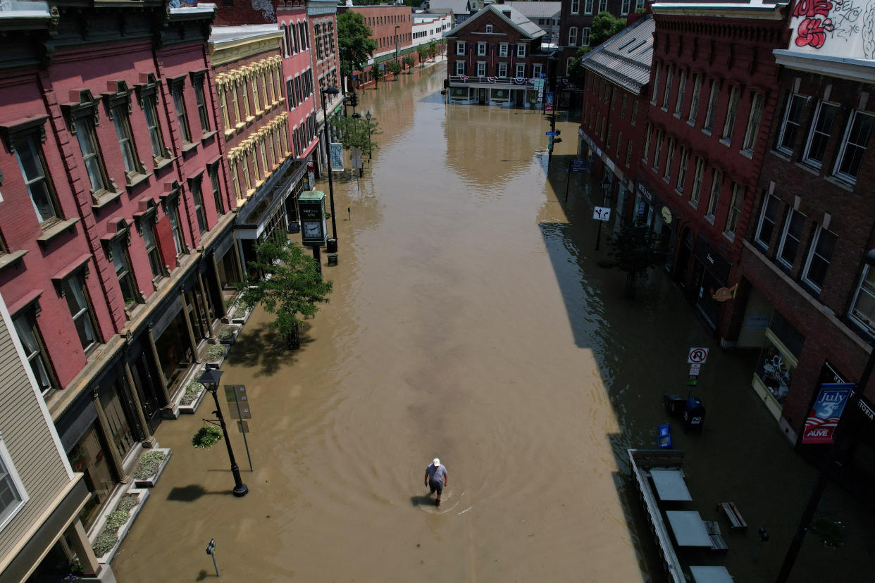 A man walks down a flooded street between brick row houses.