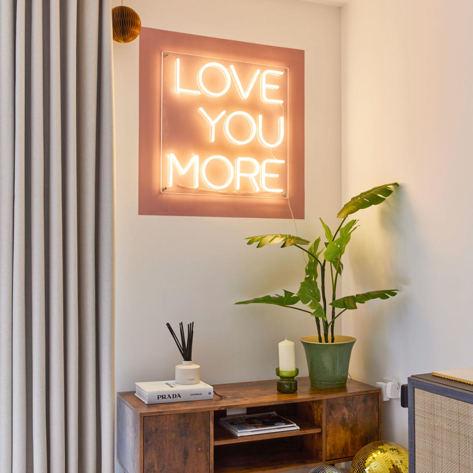 Love you more neon sign on wall above a TV unit