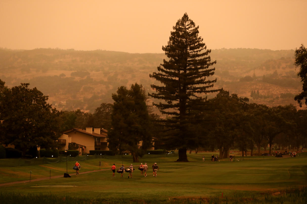 Golfers on the green in front of a hill with an orange sky.