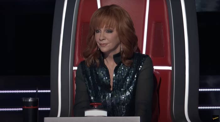 Reba in sparkling top sitting in a judge's chair on a talent show set