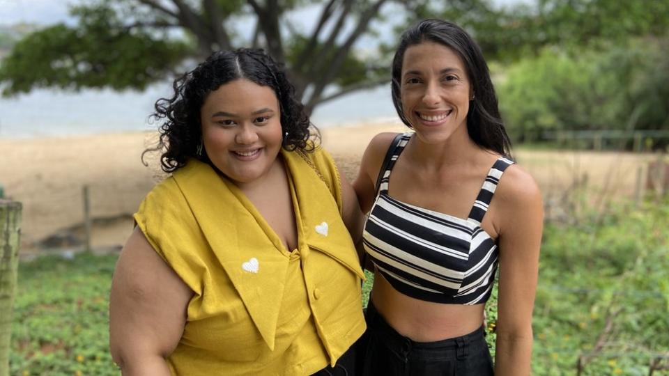 Rayane y Mariana posan sonriendo con la playa atrás.