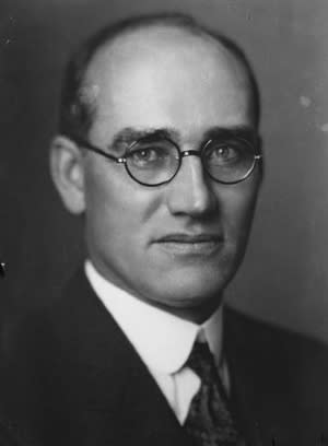 William Comstock poses for a photo. He is wearing a suit and tie, with short, balding hair and wire-rimmed glasses.