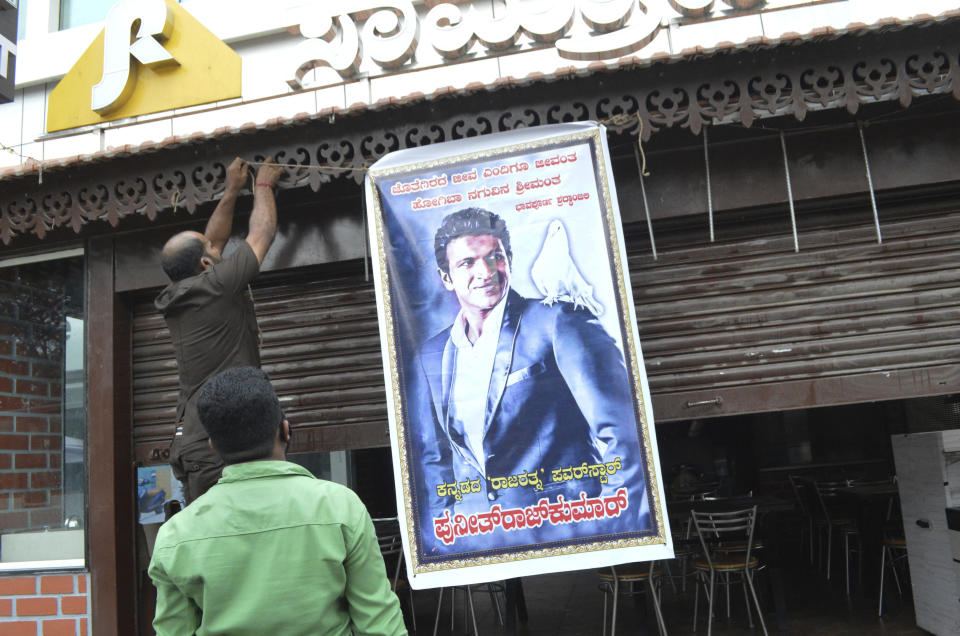 A poster of actor Puneeth Rajkumar is hung outside a hotel with closed shutters after news of the actor's death, in Bengaluru, India, Friday, Oct. 29, 2021. Rajkumar, a top star of southern Indian regional films, died on Friday after a massive heart attack, a hospital statement said. He was 46. Rajkumar was rushed to Vikram hospital in Bengaluru, the capital of southern Karnataka state, after he complained of chest and died there, the statement said. The Press Trust of India news agency said he had a two-hour workout in a gymnasium and was rushed to the hospital straight from there. (AP Photo)