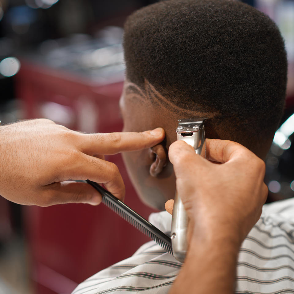 Closeup of process of trimming trendy stripes on head in barber shop. Barber keeping clipper and comb in hands and cutting hair to male sitting on chair. Concept of hairdressing and shaving.