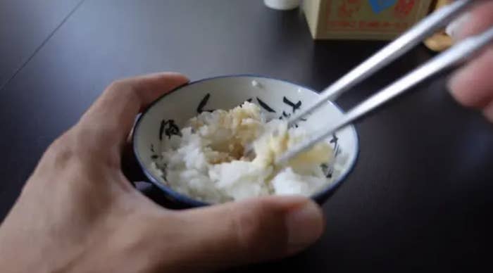 Chopsticks picking up rice in a little ramekin