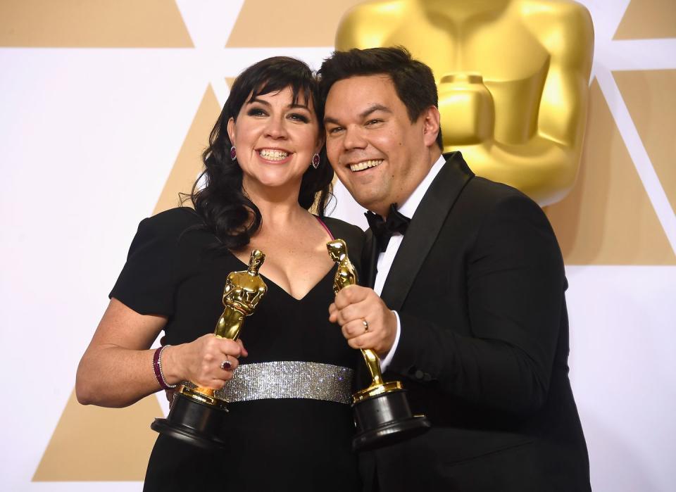 robert lopez stands to the right of his wife, kristen anderson lopez, both of whom are holding an oscar after winning best song in 2018