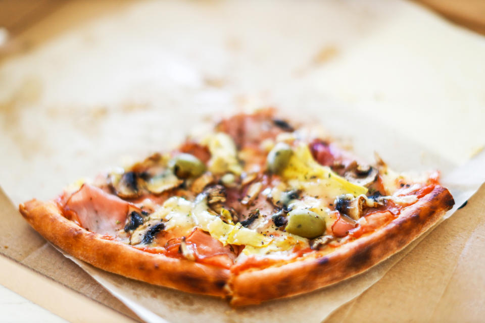 A close-up of a partially eaten pizza slice with toppings including olives, mushrooms, ham, and cheese, displayed on a piece of parchment paper