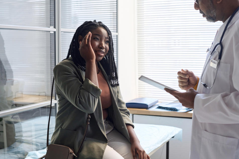 Woman in a clinic listening to a doctor holding a tablet. They are engaged in conversation