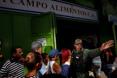 A Venezuelan soldier tries to control the crowd as people queue to buy food outside a market in Caracas, Venezuela July 19, 2016. REUTERS/Carlos Garcia Rawlins