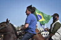 Brazil's President Jair Bolsonaro rides a horse greeting supporters outside the presidential palace in Brasilia, Brazil, Sunday, May 31, 2020. Bolsonaro mounted a horse from police that were guarding supporters of his government gathered outside the Planalto Palace. (AP Photo/Andre Borges)