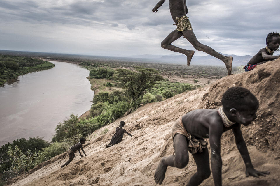 <p>Omo change: Indigenous Karo children play in the sand on the banks of the Omo River in Ethiopia. The Karo people are entirely dependent on the river for food: both for fish and crops grown in fertile flood soil. The forest seen in the background was cleared to make way for commercial cotton plantations, July 24, 2011.<br>Ethiopia is in the midst of an economic boom, with growth averaging 10.5 percent a year — double the regional average. One of the areas most impacted by this is the Omo Valley, an area of extraordinary biodiversity along the course of the Omo River, which rises in the central Shewan highlands and empties into Lake Turkana, on the border with Kenya.<br>Some 200,000 people of eight different ethnicities live in the Omo Valley, with another 300,000 around Lake Turkana in Kenya. Many are reliant on the river for their food security: on fish in the river and lake, and on crops and pastures grown in the fertile soil deposited by annual natural floods. Gibe III Dam — at 243 meters the tallest in Africa, and generating some 1,800 MW of hydroelectric power — was built with a dual aim: to provide energy for the booming economy and for export, and to deliver an irrigation complex for high-value agricultural development. It was also said that the dam would become a tourist attraction, of socio-economic benefit. Both Ethiopian and Kenyan governments support the dam and have disputed claims of a negative environmental impact, but critics point to such adverse effects as the cessation of natural floods, diminishing biodiversity, falling water levels in Lake Turkana, and the displacement of traditional peoples who have lived for centuries in a delicate balance with the environment.<br>The photographer visited the Omo Valley during the final years of the dam’s construction, with the aim of producing a meditation on how important investments can nonetheless put the human-environment balance at risk, and on how the changes brought about by the presence of such large amounts of money disrupt existing equilibrium. (Photo: Fausto Podavini) </p>