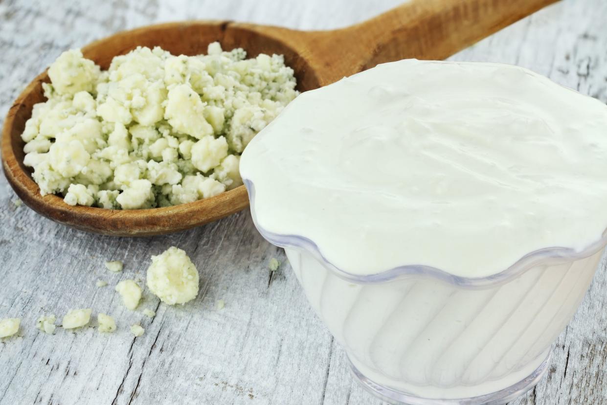 Bowl of freshly made blue cheese salad dressing with chunks of blue cheese in wooden spoon on a rustic background.