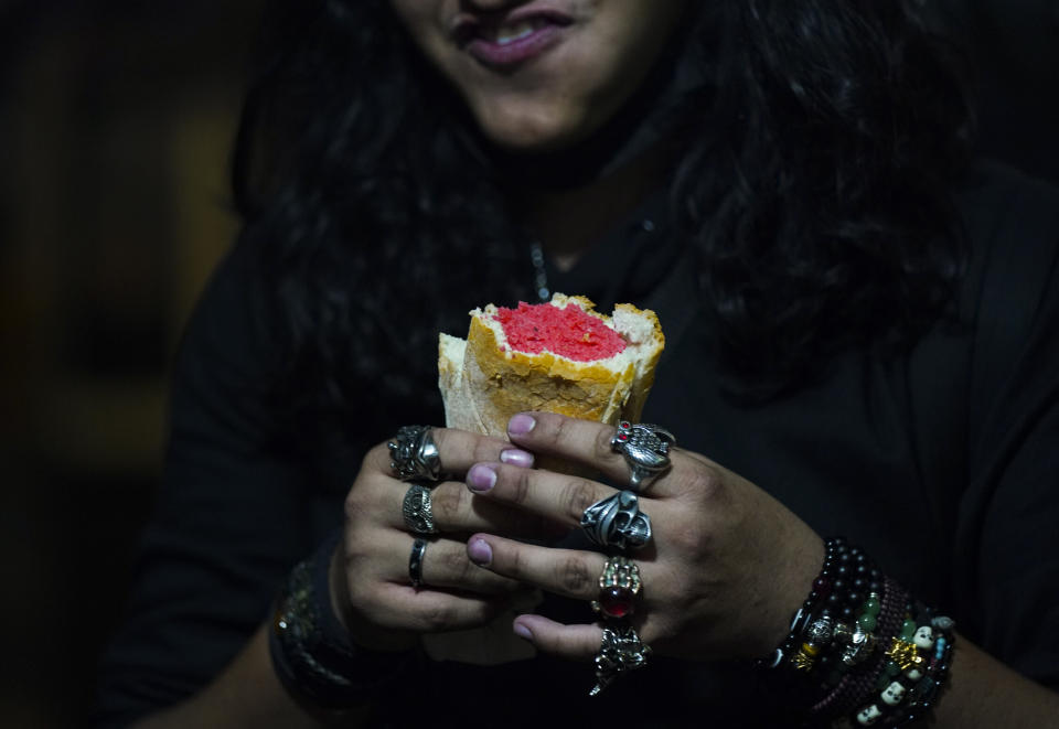 Un joven que toca la guitarra en una banda de rock toma un característico tamal de dulce color rosa antes de un concierto, en un puesto callejero de tamales en el centro de la Ciudad de México, el 26 de enero de 2023. De madrugada, los vendedores instalan sus puestos junto a estaciones de metro y en cruces en toda la ciudad, donde los tamales se preparan dentro de grandes ollas de vapor conocidas como “tamaleras”, (AP Foto/Fernando Llano)