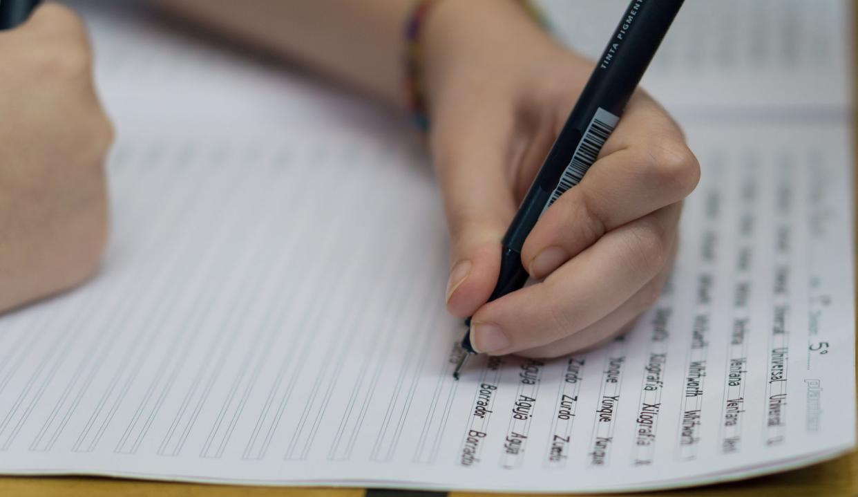 Left handed girl holding a black pen writing homework in notebook, selective focus