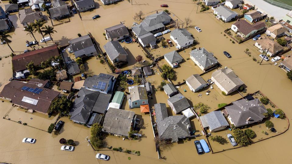 Floodwaters surround homes and vehicles in the community of Pajaro in Monterey County, Calif., on Monday, March 13, 2023. Built in the late 1940s to provide flood protection, the Pajaro River's levee has been a known risk for decades with several breaches in the 1990s. Emergency repairs to a section of the berm were undertaken in January. (AP Photo/Noah Berger)