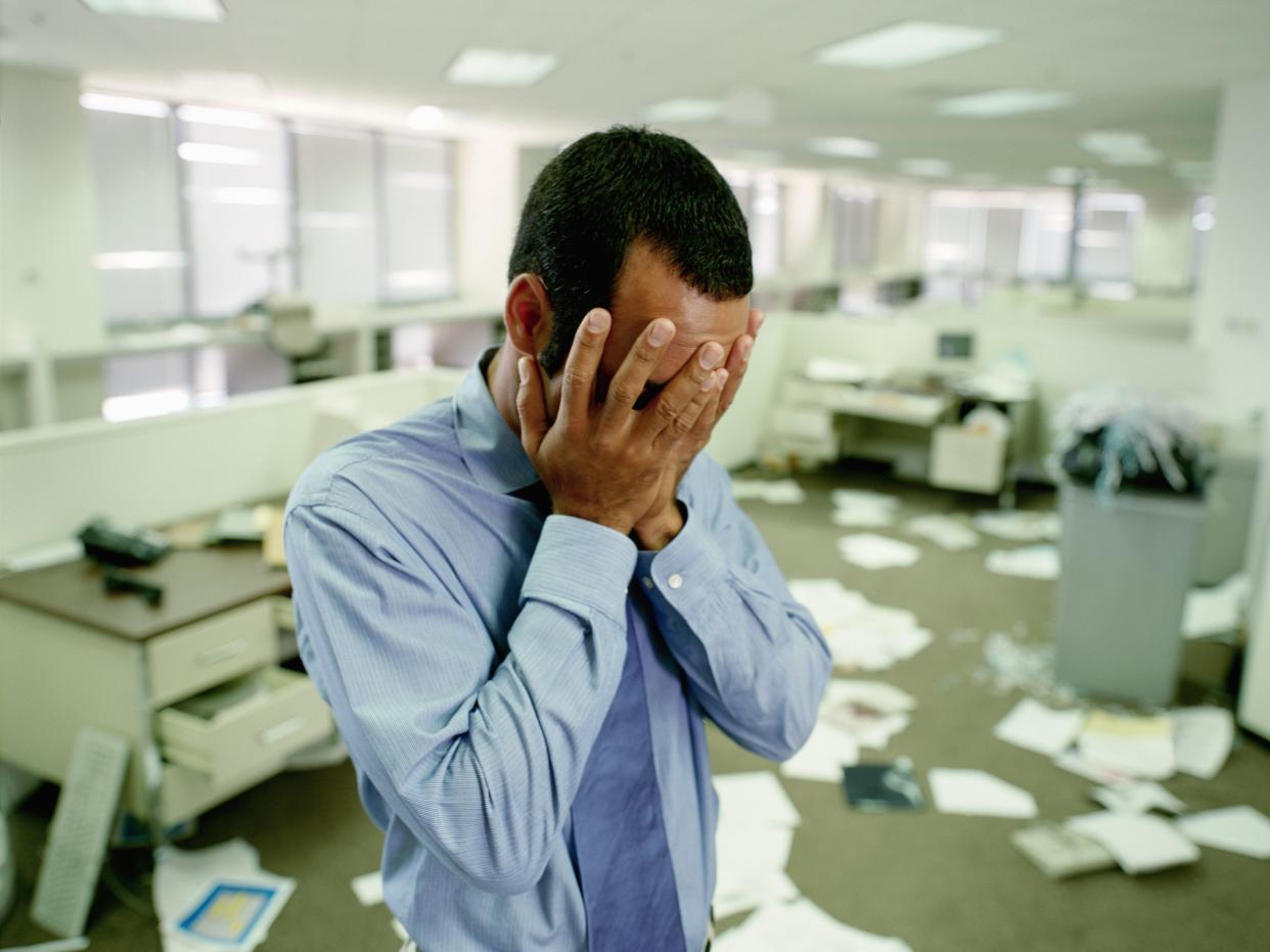 Man with head buried in his hands in a messy office.