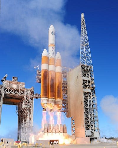 A gold and white rocket, with flames coming out of the end, attached to a concrete scaffolding.