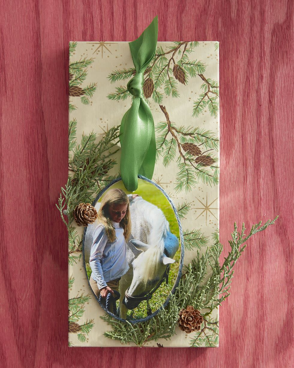 ornament made from a picture of a young girl with a horse, there is a piece of wrapping paper behind it and greenery around it