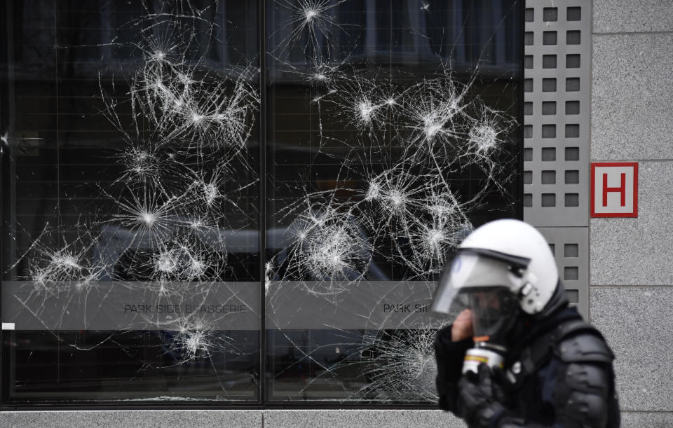 A police officer walks by a damaged building in the European Union quarter during a demonstration against COVID-19 measures in Brussels, Sunday, Jan. 23, 2022. Demonstrators gathered in the Belgian capital to protest what they regard as overly extreme measures by the government to fight the COVID-19 pandemic, including a vaccine pass regulating access to certain places and activities and possible compulsory vaccines. (AP Photo/Geert Vanden Wijngaert)