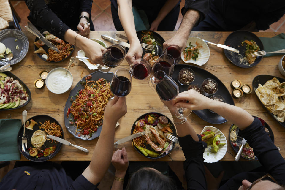 a group of people eating together at a table with several plates of food and toasting