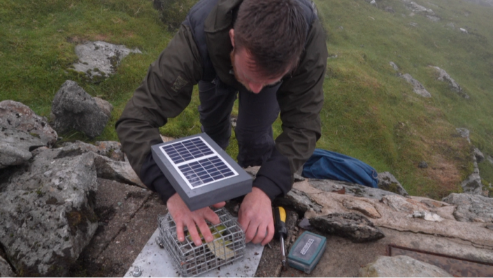Alec Young places a banana skin inside the banana-cam cage at a location on the summit of Snowdon