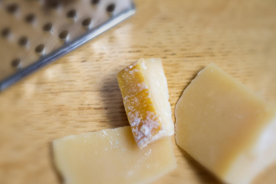 Close-up of two pieces of Parmesan cheese next to a metal grater on a wooden surface