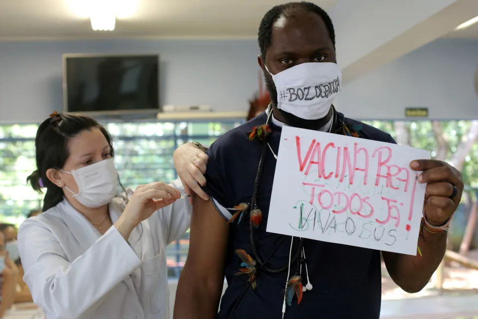 An Indigenous man receives the second dose of Sinovac&#39;s CoronaVac coronavirus disease (COVID-19) vaccine at a health station, as he holds a cardboard that reads: &#39;&#39;Vaccine for all now&#39;&#39; and wears a protective face mask that reads: &#39;&#39;#BozoGenocidal&#39;&#39; in reference of Brazil&#39;s President Jair Bolsonaro, in Guarulhos, near Sao Paulo, Brazil March 2, 2021. REUTERS/Carla Carniel