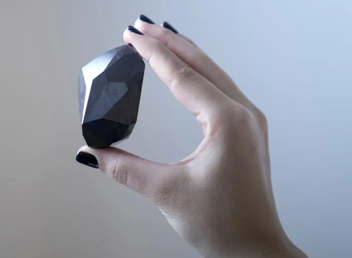 An employee of Sotheby's Dubai presents a 555.55 Carat Black Diamond "The Enigma" to be auctioned at Sotheby's Dubai gallery, in Dubai, United Arab Emirates, Monday, Jan. 17, 2022. (AP Photo/Kamran Jebreili)