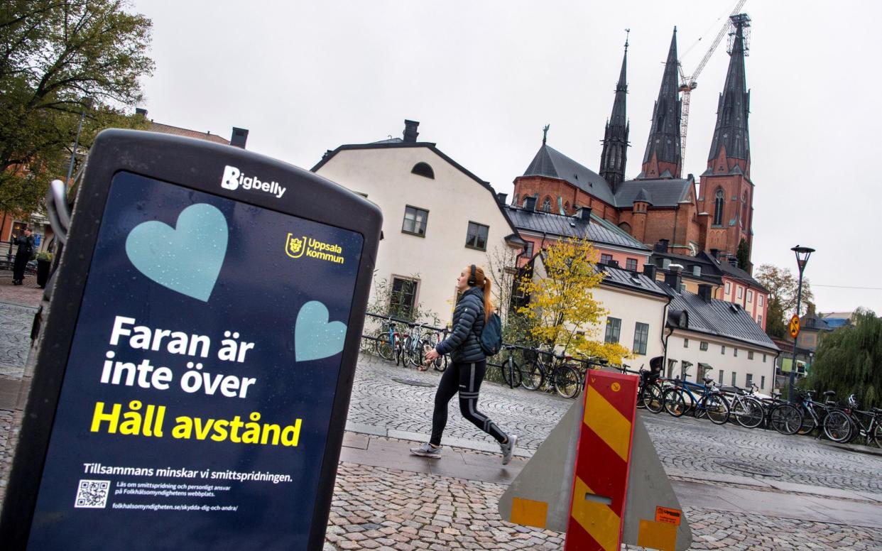 A woman walks past a Covid warning sign outside the cathedral in Uppsala - TT News Agency via Reuters