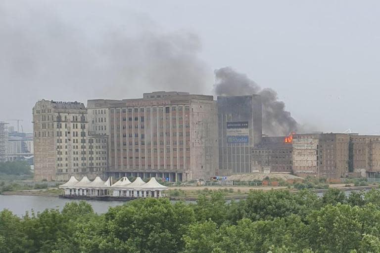 Smoke is filling the sky above the Millennium Mills building as firefighters battle a blaze. London Fire Brigade is at the scene, near London City Airport, and stated half of a derelict factory is alight. A statement said: "Ten fire engines and around 70 firefighters have been called to a fire at a derelict factory in Mill Road in Silvertown."Around half of one section of the building is currently alight."Residents and businesses in the area are advised to keep windows and doors closed as a precaution while firefighters continue to tackle the fire."The alarm was raised at 6.05pm and the fire was under control by 8.49pm. The brigade said the location was reported to it as Millennium Mills. Millennium Mills is an old flour mill on the south side of the Royal Victoria Dock. It has appeared in numerous films and tv programmes. Scenes for Ashes to Ashes and Trance were shot at the location. It has also been used as a setting in music videos for bands such as The Smiths, Arctic Monkeys and Coldplay.