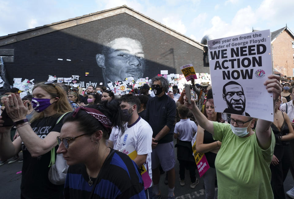 FILE - A protester holds-up a banner bearing an image of George Floyd during an anti-racism protest, near a mural of Manchester United striker and England player Marcus Rashford, on the wall of the Coffee House Cafe on Copson Street, in Withington, Manchester, England, Tuesday July 13, 2021. The mural was defaced with abusive graffiti in the wake of England losing the Euro 2020 soccer championship final match to Italy. (AP Photo/Jon Super, File)