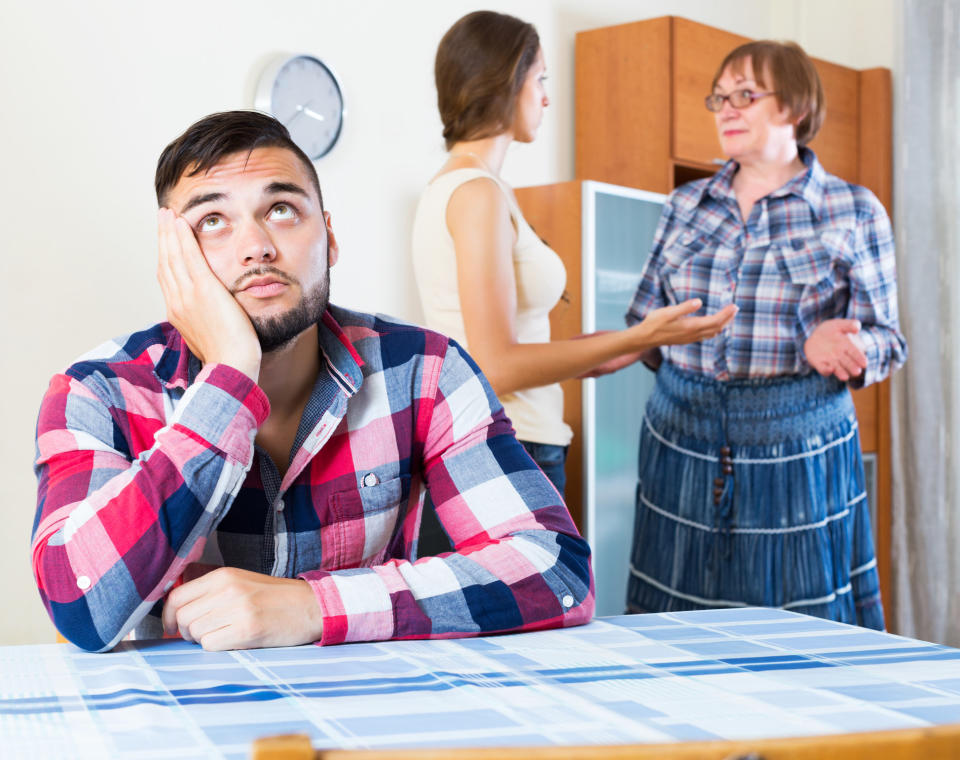 Man rolling eyes at the table while his girlfriend and her mother are talking behind him