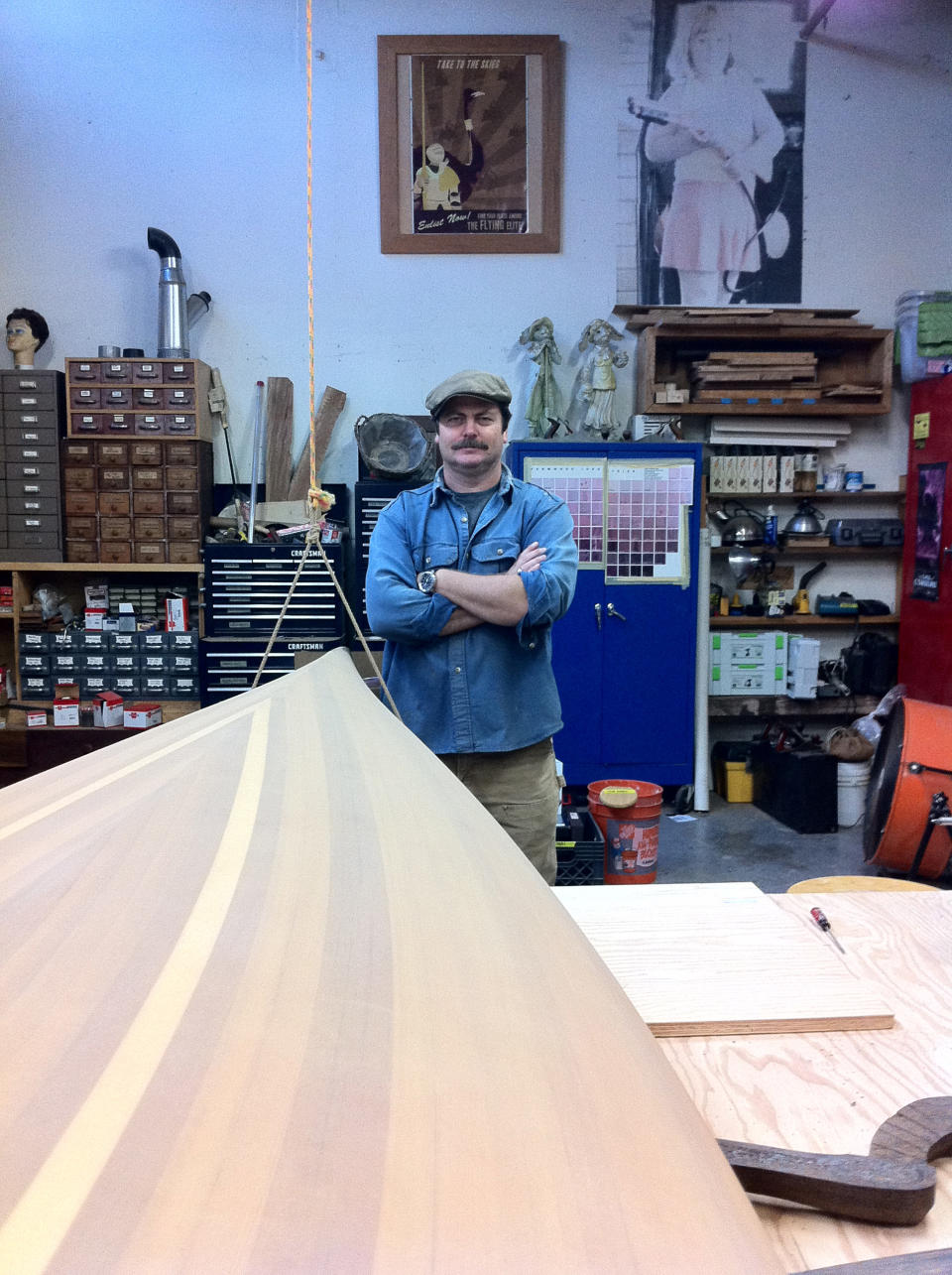 In this February 2012 image released by Jessica Glazer, Nick Offerman, who plays Ron Swanson on NBC's "Parks & Recreation," stands next to one of two canoes he built as shown in his Woodworking Studio in Los Angeles. Building boats requires a particular kind of commitment. It's complex and expensive. It can take months or years. And it can be addictive, working out in the garage, sawdust clinging to your clothes, making mistakes and finding the solutions yourself. (AP Photo/Jessica Glazer)