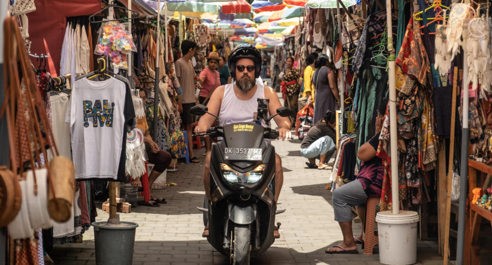 Man riding motorbike through Bali market. 