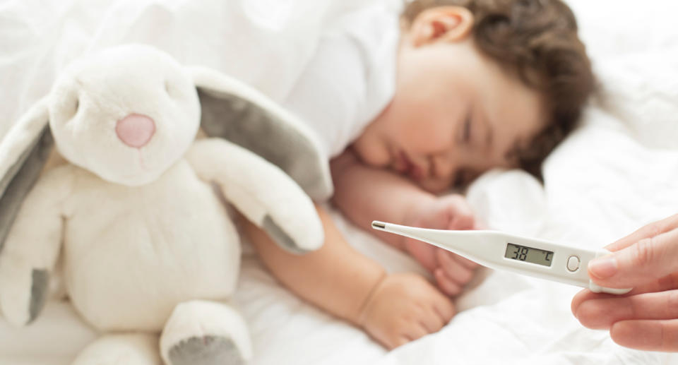 Sick toddler with a bunny, as hand holds thermometer saying 38C.