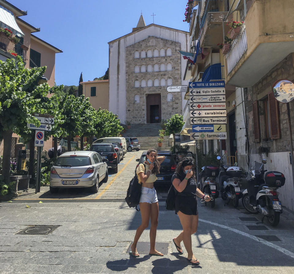Two women walk in front of Saints Lorenzo and Mamiliano Church at the Giglio Island, Italy, Wednesday, June 24, 2020. Some 50 local mourners filled the pews for a funeral in this church, including a man from the continent that had COVID-19 infection, recalled the pastor, Rev. Lorenzo Pasquotti. “After the funeral, there were greetings, hugging and kissing,” as always. Then came the procession to the cemetery, where “there were more hugs and kisses.” Yet, “none of us had any sign” of COVID-19 in the days to follow, said Pasquotti. “No one was sick. No symptoms that can make you think you were infected.” (AP Photo/Paolo Santalucia)